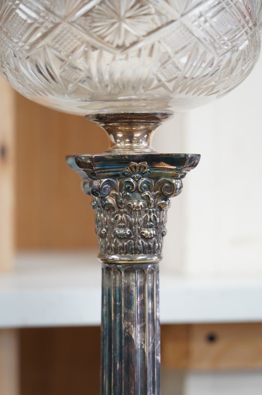 A silver plated oil lamp in the form of a Corinthian column with cut glass reservoir, 76cm high. Condition - fair to good, missing chimney and shade